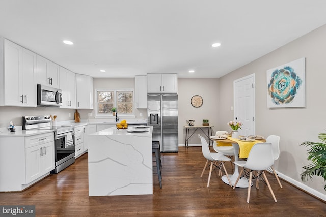 kitchen with a breakfast bar, appliances with stainless steel finishes, white cabinetry, a center island, and light stone counters