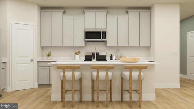 kitchen featuring a breakfast bar, range, an island with sink, light hardwood / wood-style floors, and white cabinets