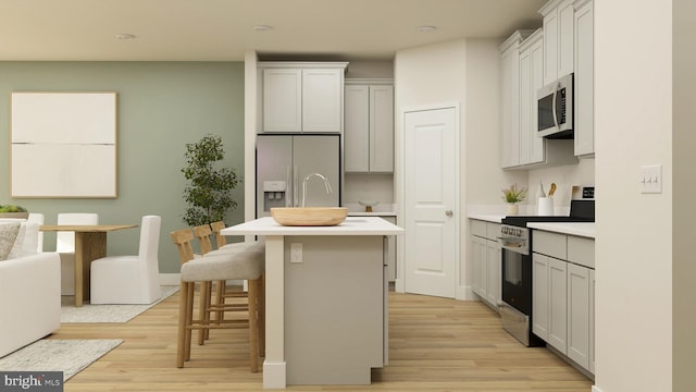 kitchen with appliances with stainless steel finishes, white cabinets, a kitchen bar, a kitchen island with sink, and light hardwood / wood-style flooring