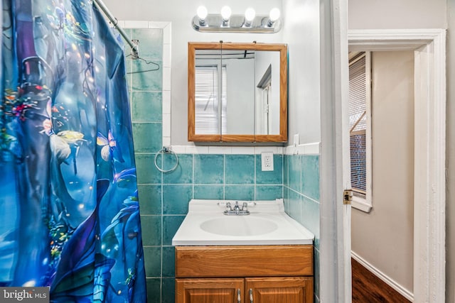 bathroom featuring walk in shower, vanity, and tile walls