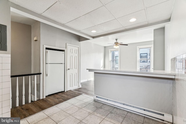 kitchen featuring tile patterned floors, a paneled ceiling, baseboard heating, white refrigerator, and ceiling fan