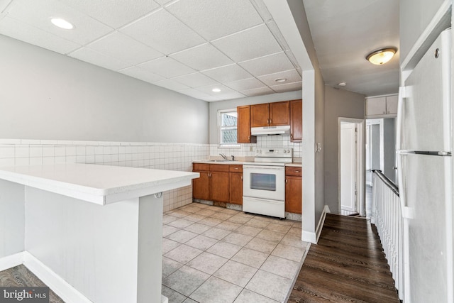 kitchen featuring a breakfast bar, sink, kitchen peninsula, a drop ceiling, and white appliances