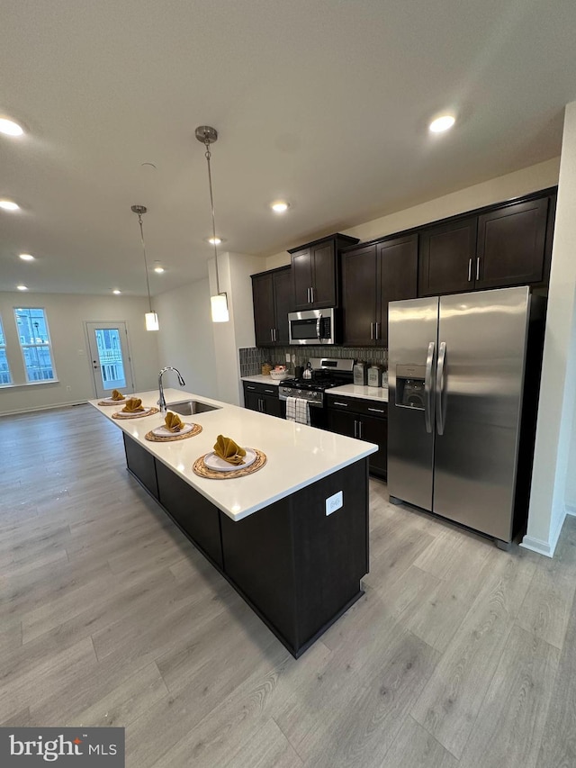 kitchen featuring sink, stainless steel appliances, tasteful backsplash, a center island with sink, and decorative light fixtures