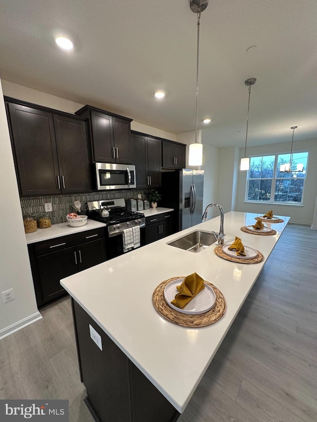 kitchen featuring sink, tasteful backsplash, pendant lighting, stainless steel appliances, and a kitchen island with sink