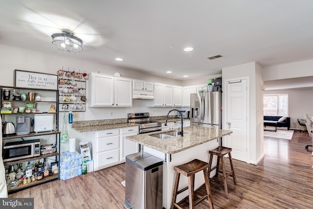 kitchen featuring sink, stainless steel appliances, light stone counters, white cabinets, and a kitchen bar