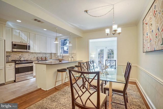 dining room featuring sink, a notable chandelier, ornamental molding, light hardwood / wood-style floors, and french doors