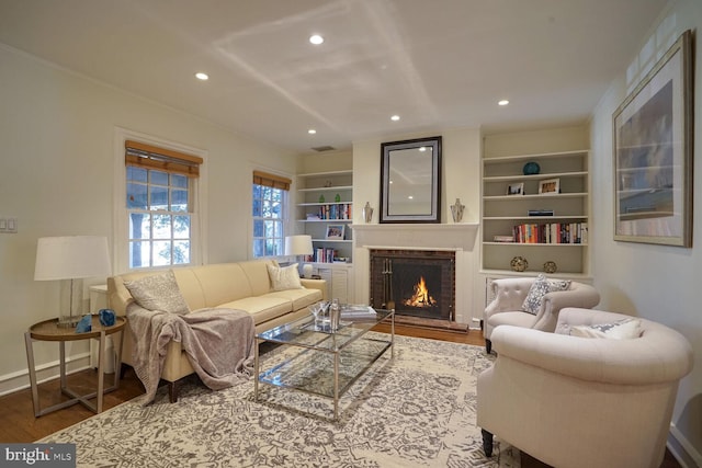 living room featuring hardwood / wood-style flooring, built in shelves, and a brick fireplace