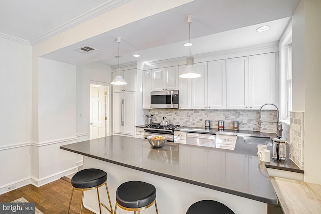 kitchen featuring pendant lighting, sink, appliances with stainless steel finishes, white cabinets, and a kitchen bar