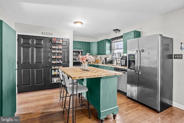 kitchen featuring butcher block countertops, light hardwood / wood-style flooring, a breakfast bar, appliances with stainless steel finishes, and green cabinetry