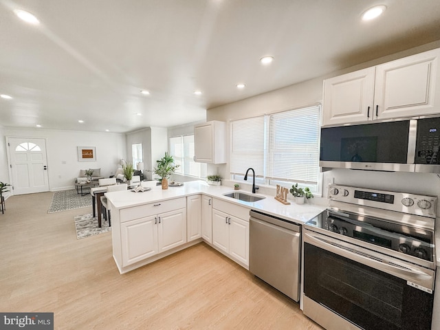 kitchen featuring appliances with stainless steel finishes, white cabinetry, sink, kitchen peninsula, and light wood-type flooring