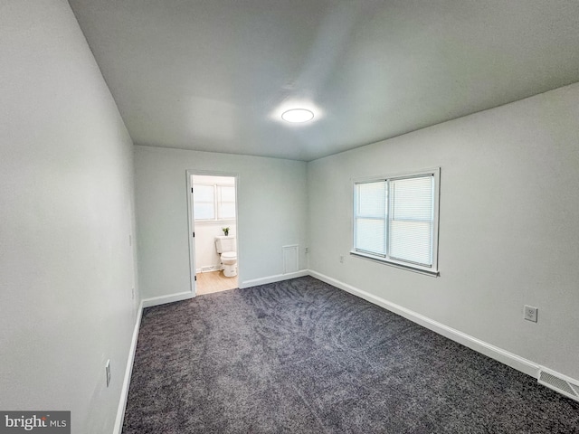 unfurnished bedroom featuring ensuite bath and dark colored carpet