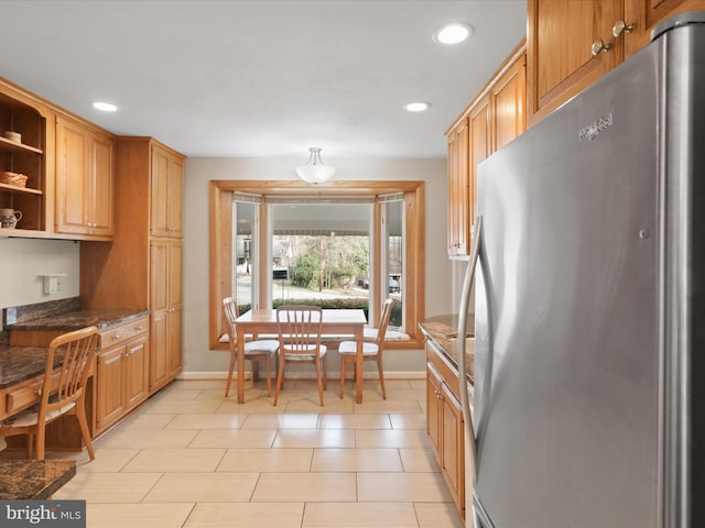 kitchen featuring built in desk, stainless steel refrigerator, dark stone counters, and light tile patterned flooring