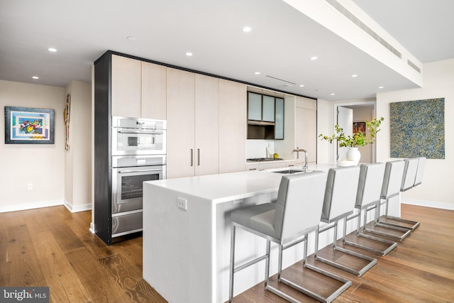 kitchen with sink, hardwood / wood-style floors, a kitchen breakfast bar, a center island with sink, and stainless steel double oven