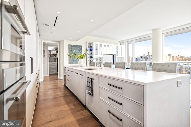 kitchen with double oven, sink, white cabinets, a large island, and light wood-type flooring