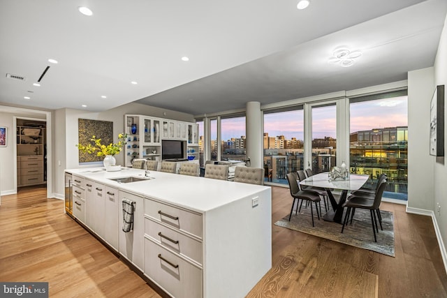 kitchen featuring sink, an island with sink, light hardwood / wood-style flooring, and white cabinets