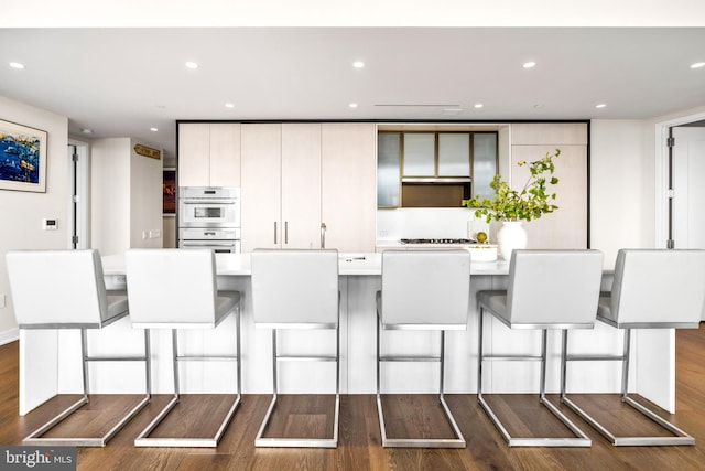 kitchen featuring dark wood-type flooring, white cabinetry, a kitchen bar, and stainless steel double oven