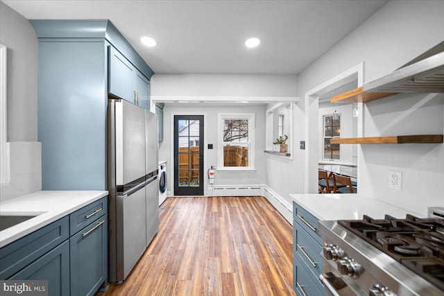 kitchen featuring hardwood / wood-style flooring, a baseboard radiator, blue cabinetry, and appliances with stainless steel finishes