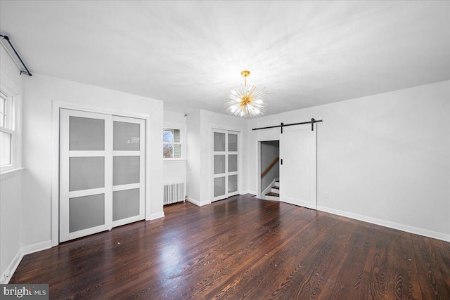 spare room featuring a barn door, dark wood-type flooring, radiator heating unit, and a chandelier