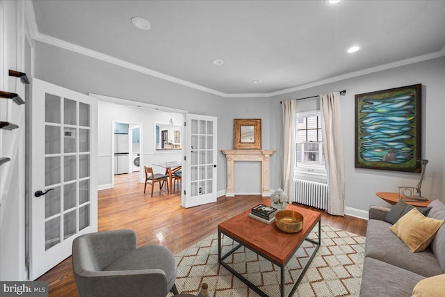 living room with radiator, crown molding, stacked washer / drying machine, wood-type flooring, and french doors