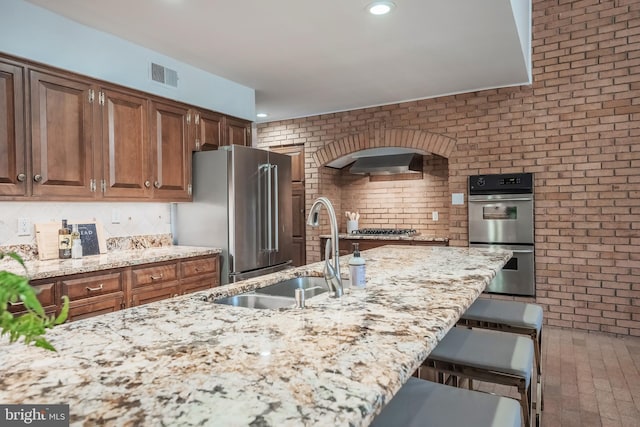 kitchen with light stone counters, stainless steel appliances, a breakfast bar, and sink