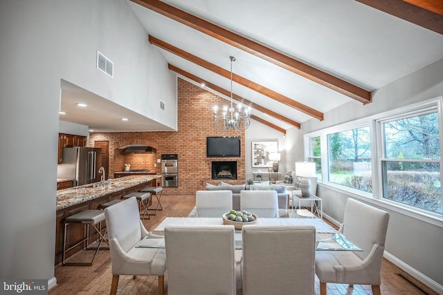 dining room with sink, an inviting chandelier, high vaulted ceiling, a brick fireplace, and beamed ceiling