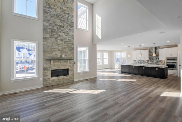 unfurnished living room with hardwood / wood-style flooring, a stone fireplace, and a high ceiling