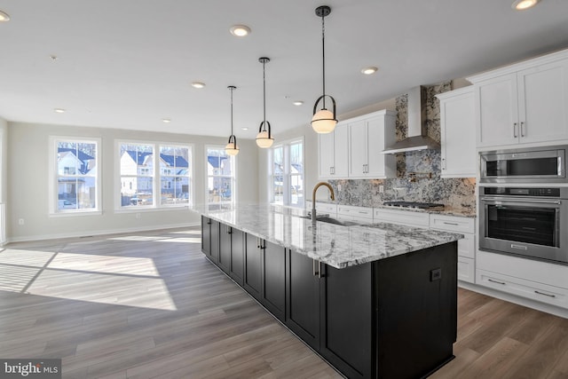 kitchen with pendant lighting, white cabinetry, a large island with sink, stainless steel appliances, and wall chimney exhaust hood