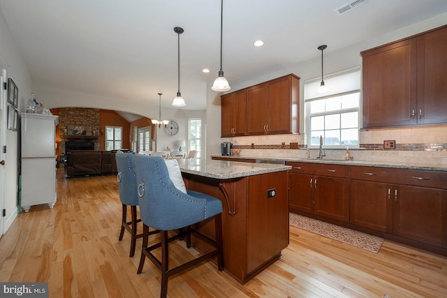 kitchen with a kitchen island, a breakfast bar, open floor plan, light stone countertops, and a sink