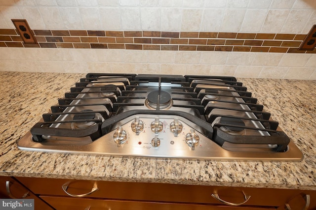 room details featuring stainless steel gas cooktop, brown cabinetry, decorative backsplash, and light stone countertops