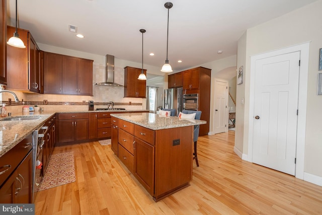 kitchen featuring pendant lighting, stainless steel appliances, a kitchen island, a sink, and wall chimney exhaust hood