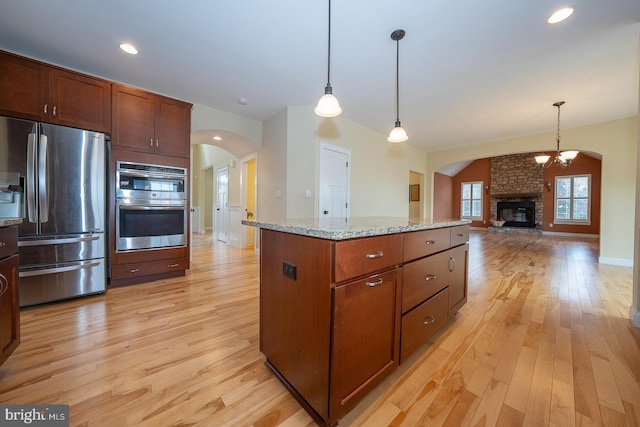 kitchen featuring a center island, light wood-style flooring, appliances with stainless steel finishes, open floor plan, and light stone countertops