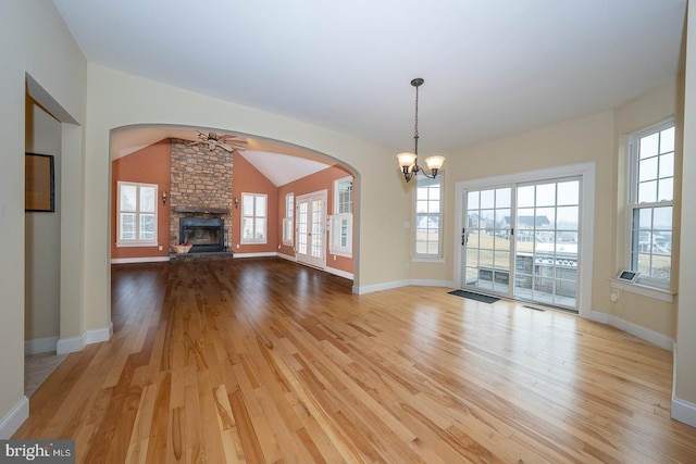 unfurnished living room featuring baseboards, vaulted ceiling, light wood-type flooring, a fireplace, and ceiling fan with notable chandelier