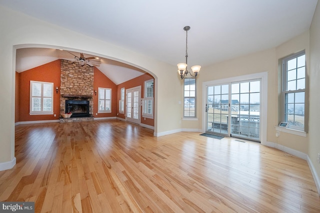 unfurnished living room with light wood finished floors, vaulted ceiling, a healthy amount of sunlight, a fireplace, and ceiling fan with notable chandelier