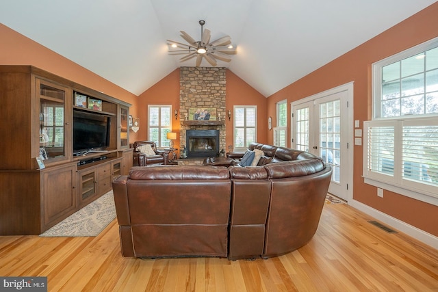 living room with visible vents, ceiling fan, a stone fireplace, and light wood finished floors