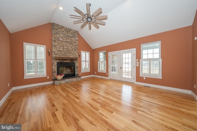 unfurnished living room with ceiling fan, high vaulted ceiling, a stone fireplace, baseboards, and light wood finished floors