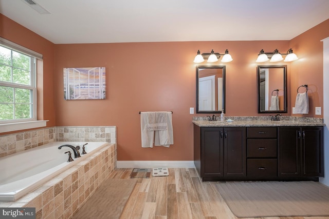 full bath featuring double vanity, baseboards, visible vents, a garden tub, and a sink