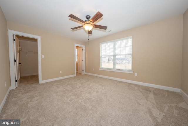 unfurnished bedroom featuring light carpet, baseboards, a ceiling fan, a spacious closet, and a closet