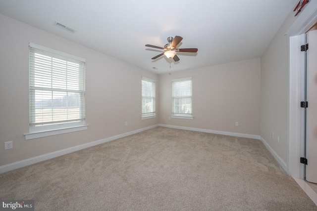 spare room featuring light carpet, a ceiling fan, visible vents, and baseboards