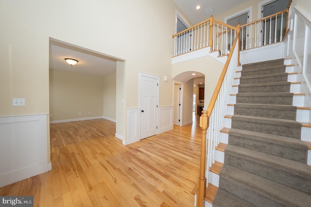 entryway featuring arched walkways, a wainscoted wall, stairway, wood finished floors, and a high ceiling