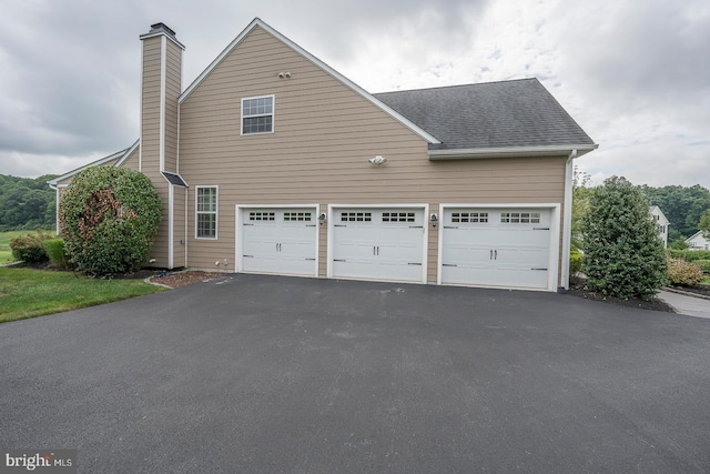 exterior space with a garage, aphalt driveway, roof with shingles, and a chimney