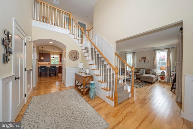 foyer entrance with stairway, a high ceiling, arched walkways, and wood finished floors