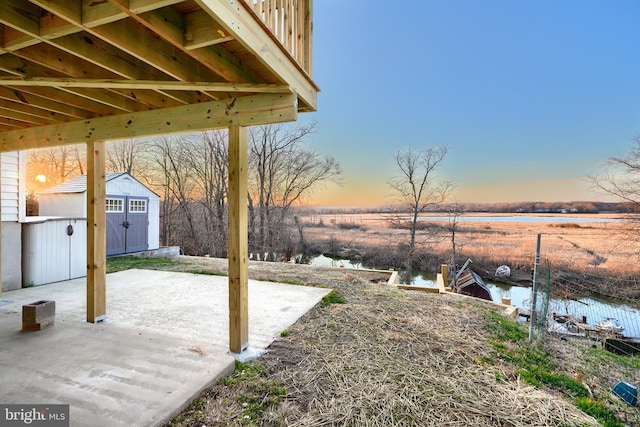 yard at dusk featuring a patio, a water view, and a shed