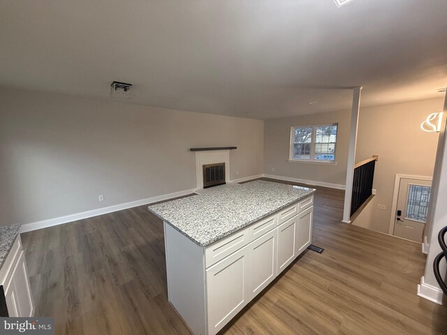 kitchen with white cabinets, dark hardwood / wood-style flooring, a center island, light stone countertops, and an inviting chandelier