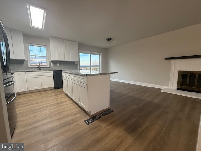 kitchen featuring sink, white cabinets, light hardwood / wood-style floors, light stone countertops, and a brick fireplace