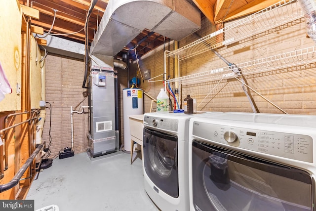 clothes washing area featuring heating unit, brick wall, washer and clothes dryer, and water heater