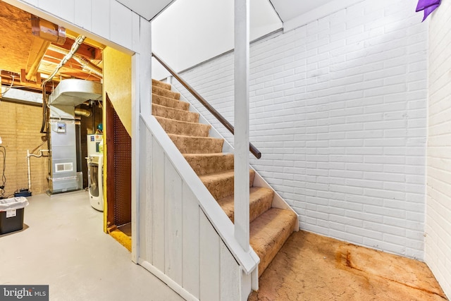 staircase featuring brick wall and concrete floors