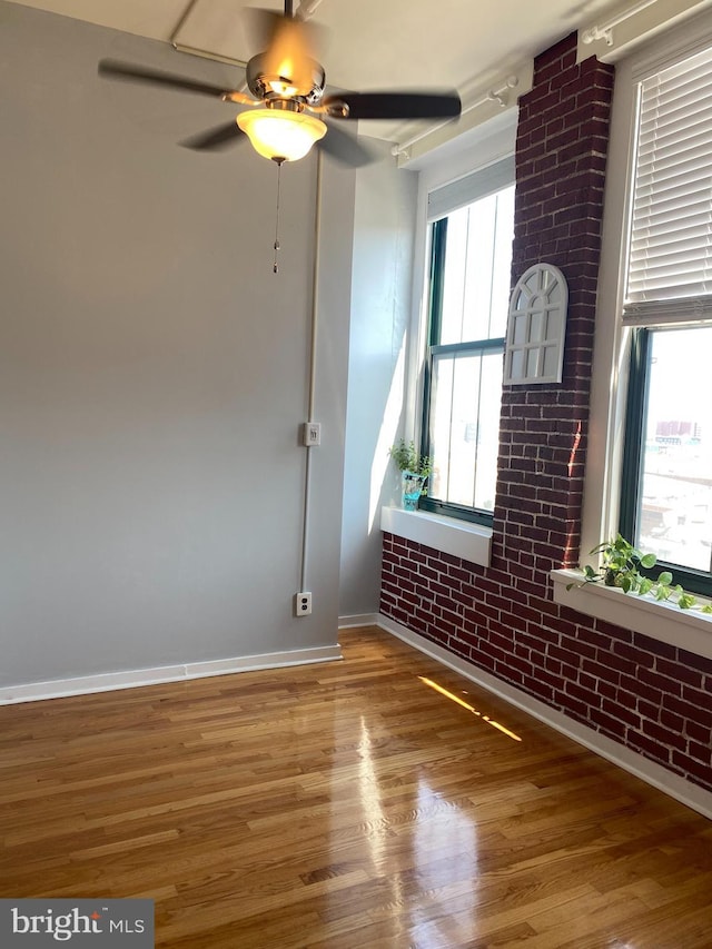 unfurnished room with hardwood / wood-style floors, a wealth of natural light, ceiling fan, and brick wall