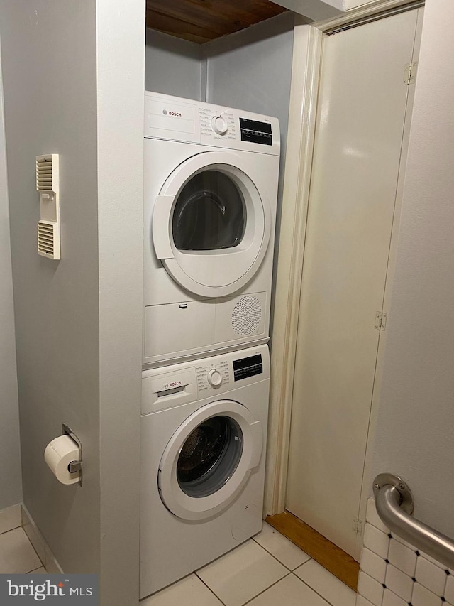 laundry area with light tile patterned flooring and stacked washing maching and dryer