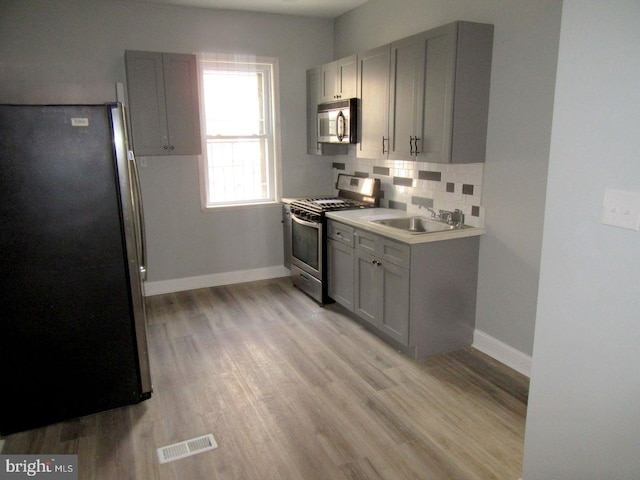 kitchen with stainless steel appliances, light hardwood / wood-style floors, sink, and decorative backsplash