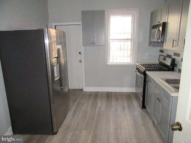 kitchen with gray cabinets, appliances with stainless steel finishes, and light wood-type flooring